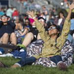 People wearing solar eclipse glasses sit in the grass to view the 2017 total solar eclipse over North America