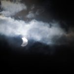 Solar eclipse through misty clouds and a dark sky.