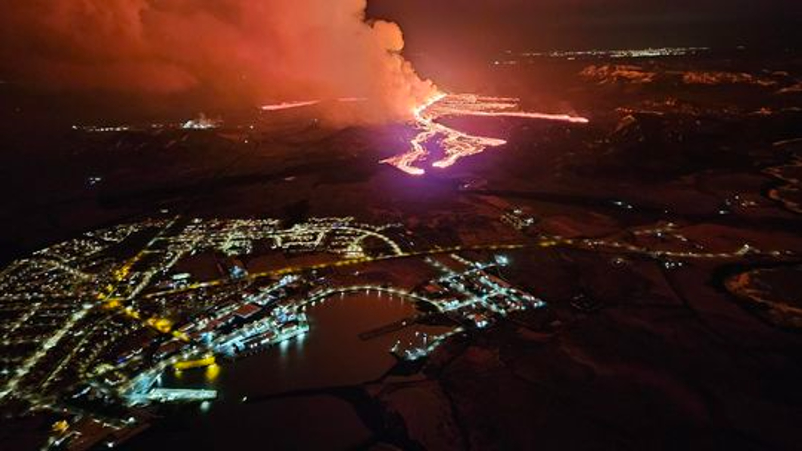 Извержение вулкана ночью с прибрежным городом на переднем плане