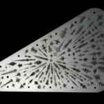 Image of one side of the commerative plate which is a silver-color, against a black background. The plate appears to have lots of symbolic markings across it and is the shape of a right-angled triangle