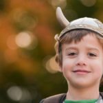 young boy smiles at the camera wearing a plastic viking helmet
