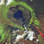 A satellite photo of a volcano with a crater lake and lava bleeeding down the side of its tree-covered slopes
