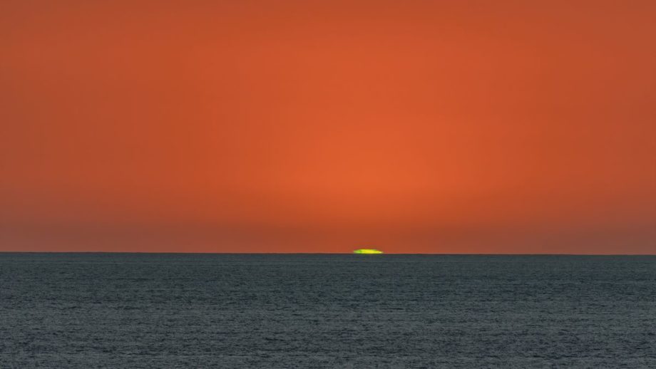 A photograph of a sunset over the ocean with a green flash around the sun.