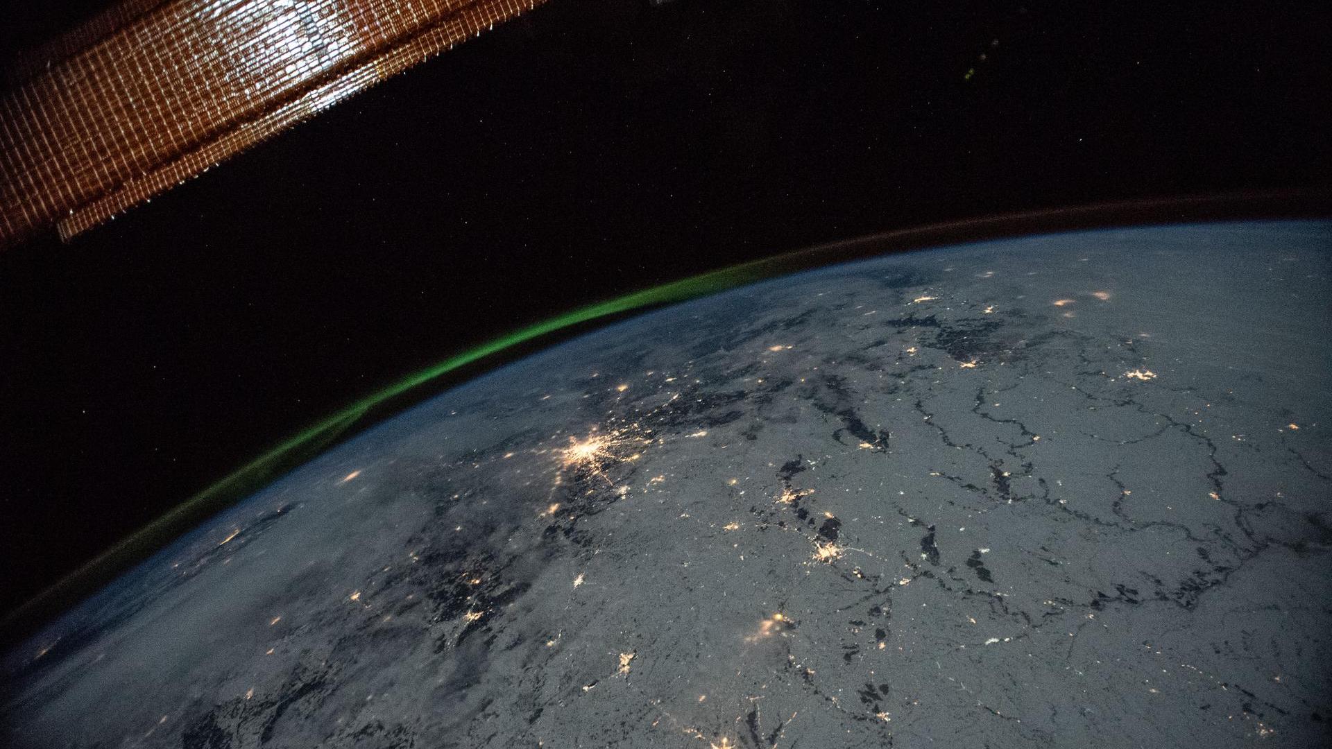 фотография зеленого полярного сияния со сверкающими огнями города, сделанная с Международной космической станции.