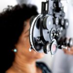 Mature woman is shown having her eyes tested by an opthalomogist. A black device is in front of her eyes which is in focus. The rest of the image is blurred