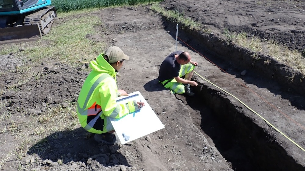 Двое мужчин работают на раскопках рядом с ямой в земле.