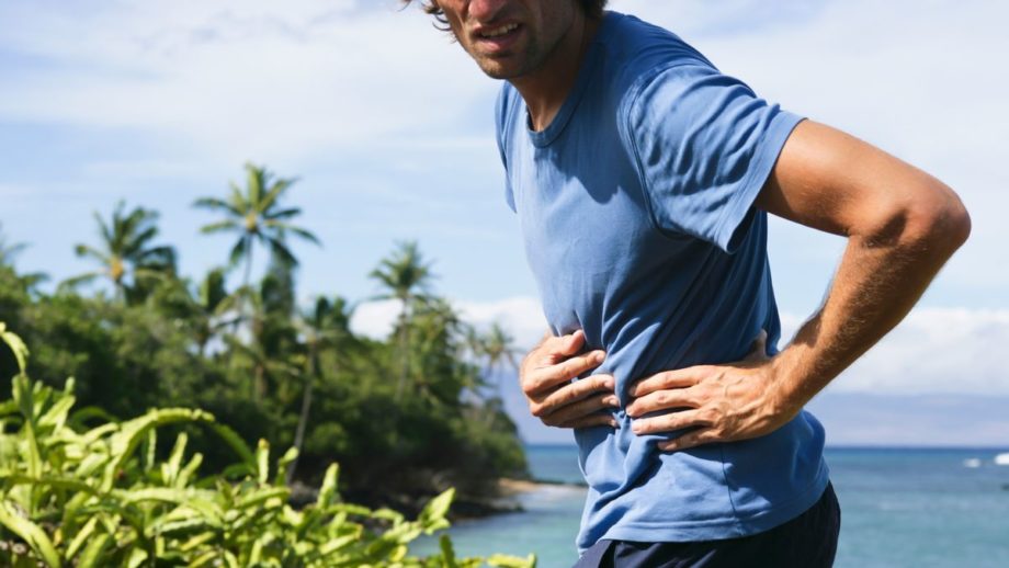 photo of a man running outside along a beach, holding his side as if in pain