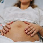 close up on the exposed belly of a pregnant woman propped up on a hospital bed and wearing a gown